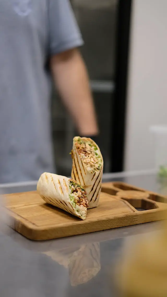 A man standing in front of sliced burrito placed on a wooden chopping board.