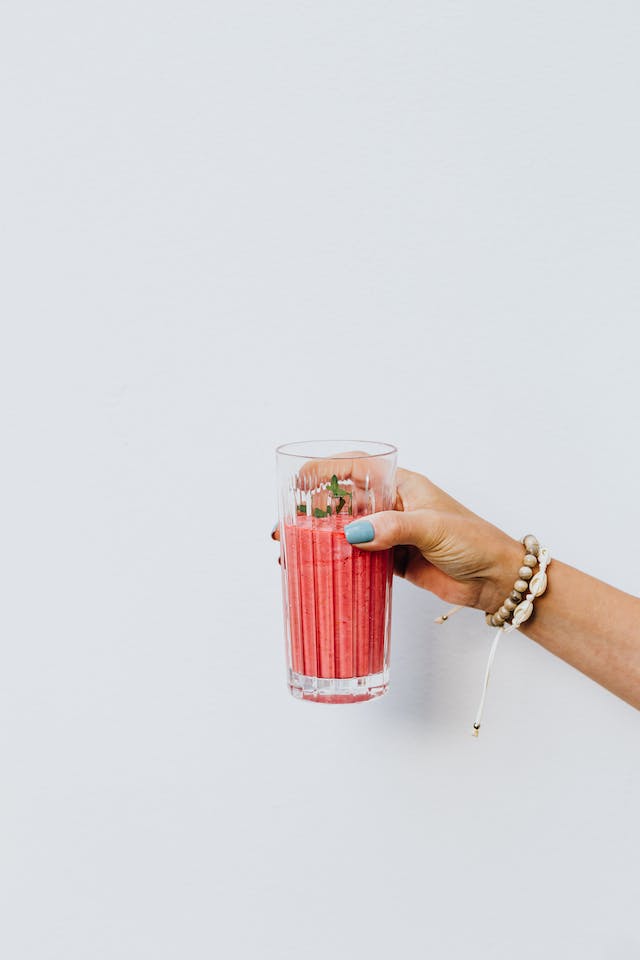 A close-up shot of a woman's manicured hands holding a pink smoothie.