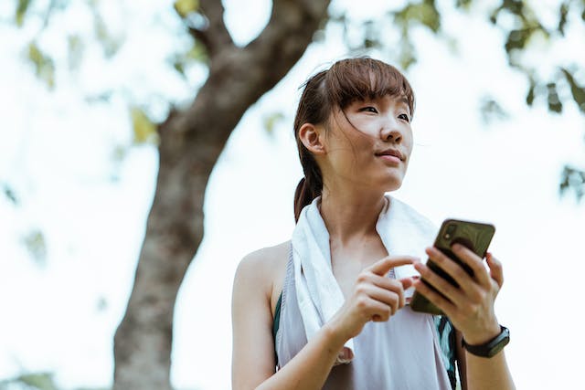 A woman with a hand towel around her neck holding her smart phone.