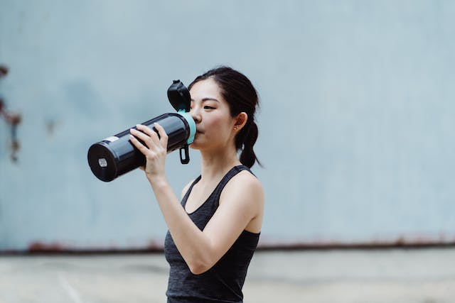 A woman in sports attire drinking from a bottle.