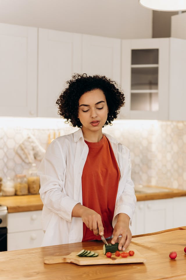 A woman slicing a piece of cucumber in her kitchen.