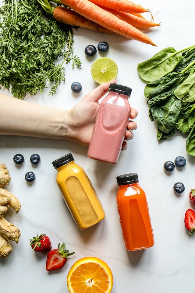 Red, orange, and pink bottled smoothies framed with a variety of vegetables
