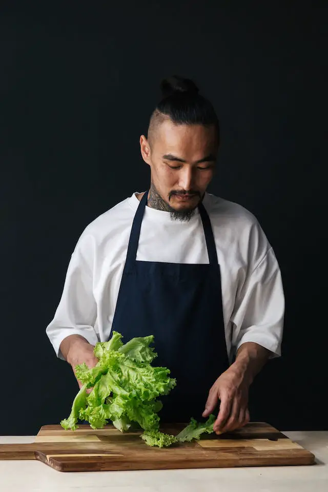A man in apron laying lettuce leaves on a wooden chopping board.