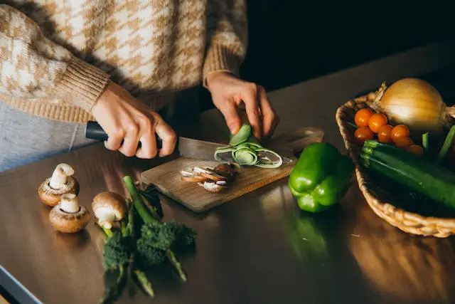 A woman slicing a broccoli on a wooden chopping board.