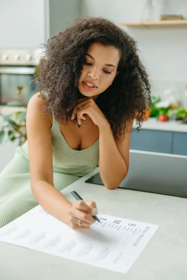 A curly-haired woman in green dress trying to make a weekly plan.