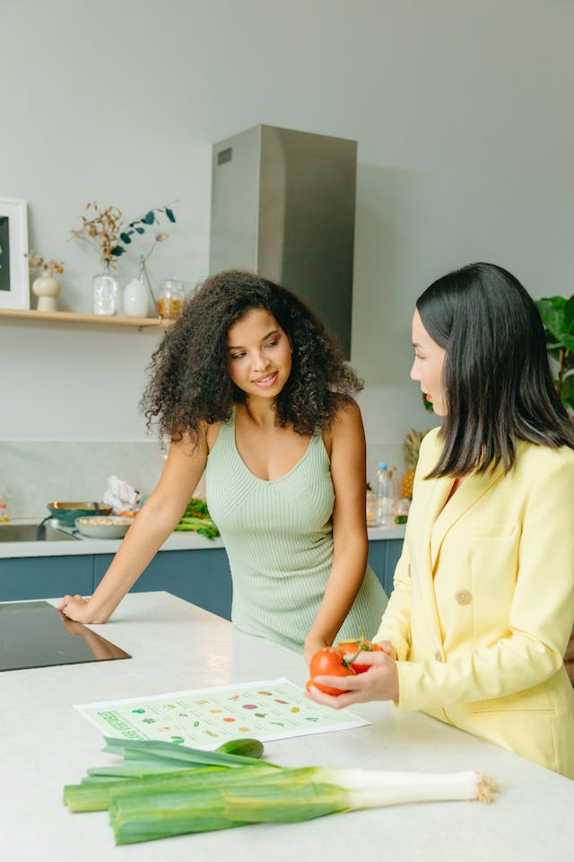 A nutritionist educating a curly-haired client while holding a couple of pieces of tomato.