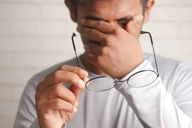 A frustrated man holding a pair of glasses and the other hand covering his eyes.