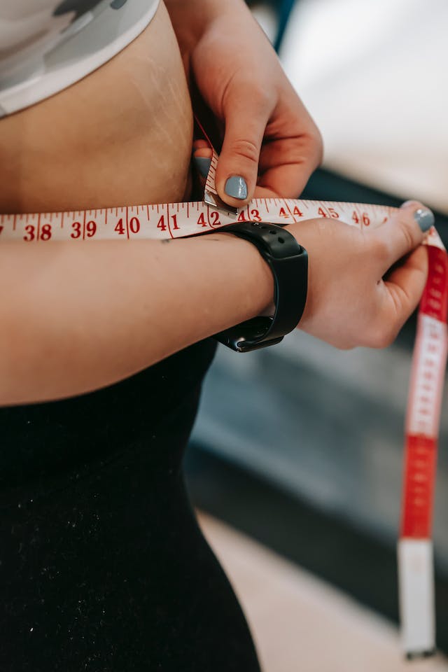 A woman measuring her waist using a tape measure.
