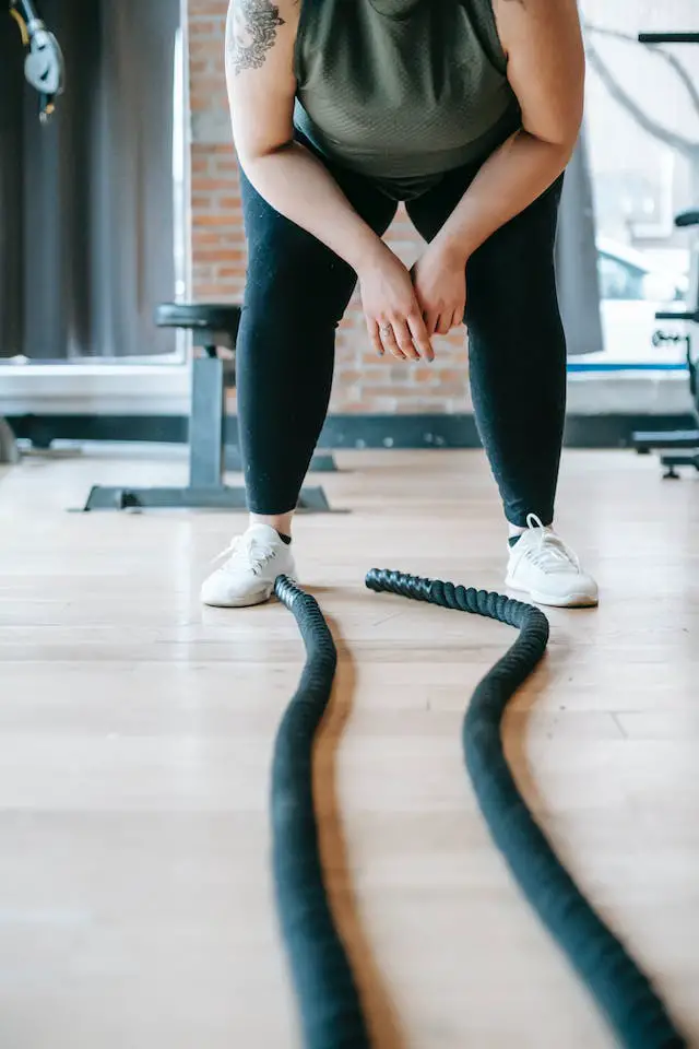 A woman resting in a slightly crouched position after exercising with battle ropes.