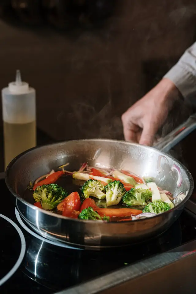 A person holding a stainless steel cooking pan with sauteed vegetables in it.