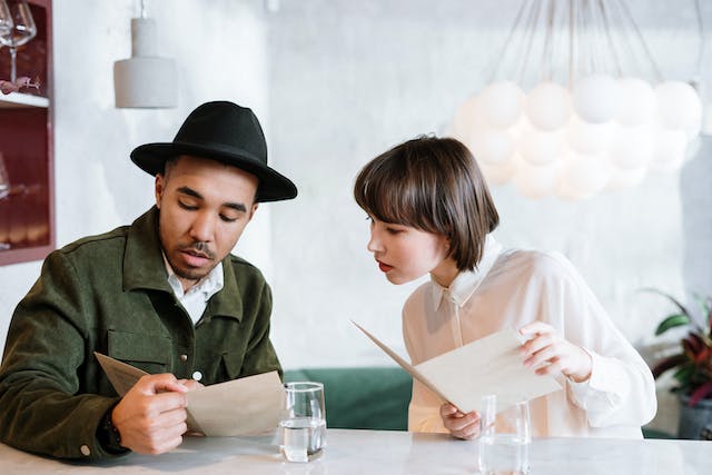 A man in green blazer and a woman in white shirt looking at their menu.