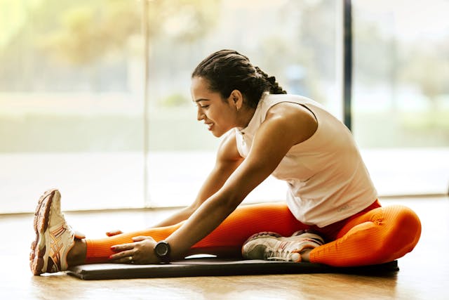 A woman in sports clothes stretching out her leg on the floor.