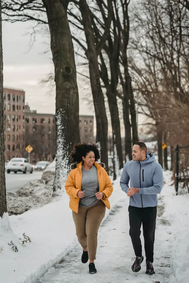 A woman and a male coach running on a snowy day at a city park.