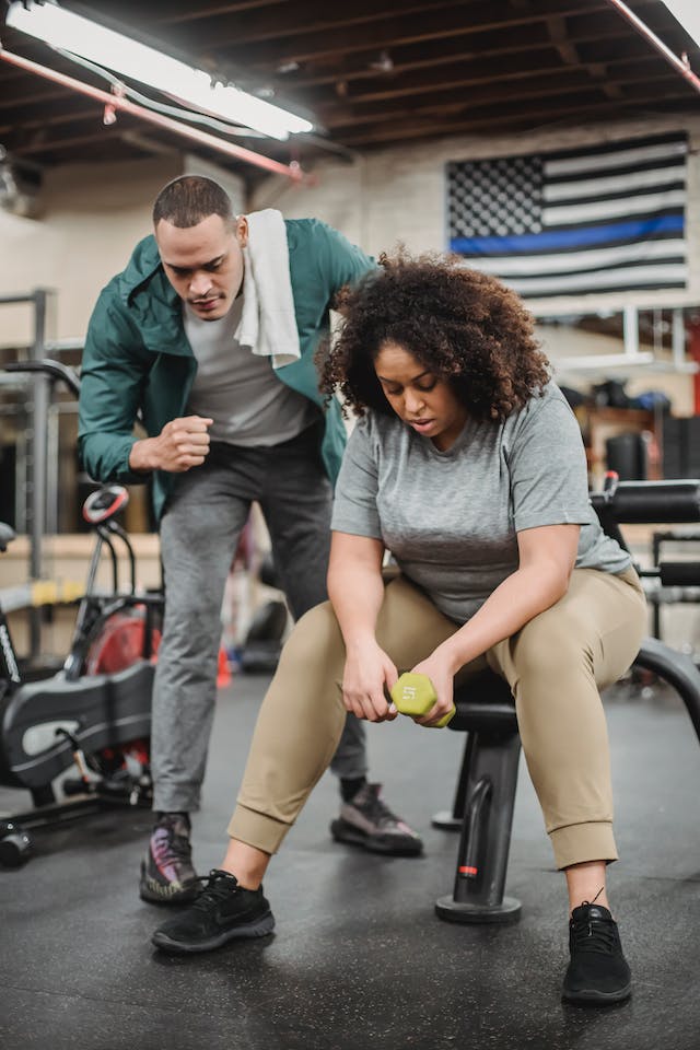 A coach encouraging his client to continue working out using a small dumbbell.