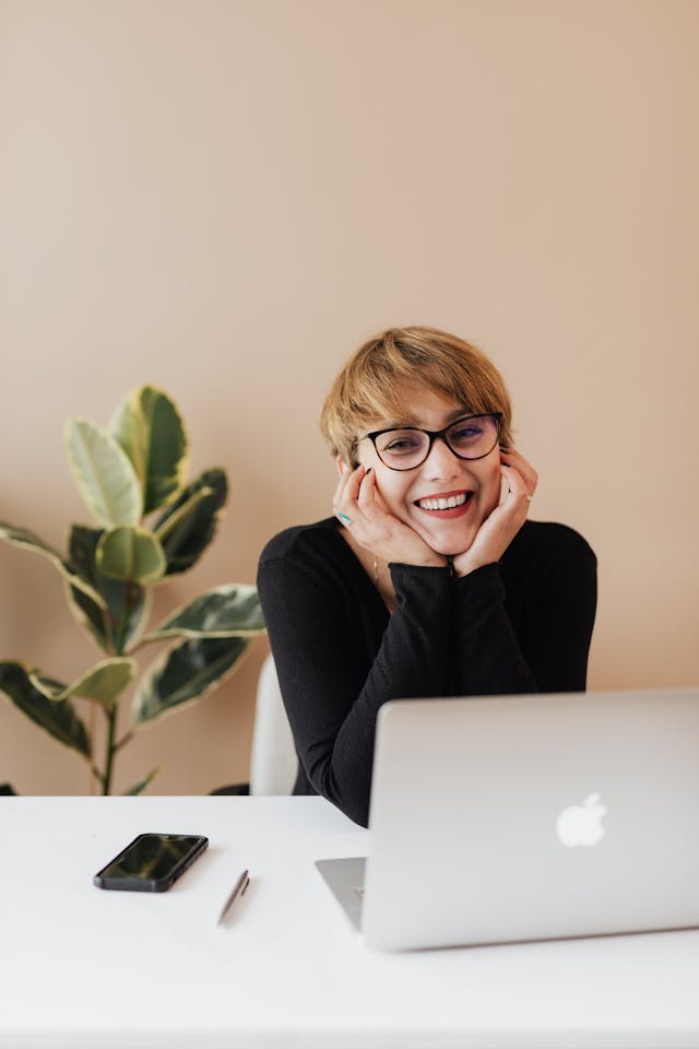 A short-haired woman smiling in front of her laptop.