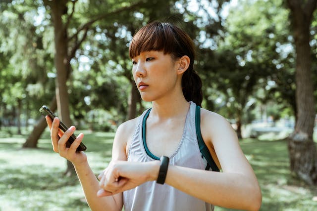 A woman in sports attire looking at her smart phone and smart watch.