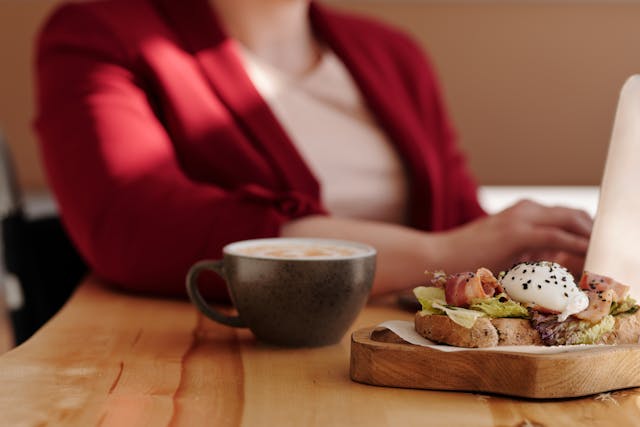 A woman working on her laptop with coffee and a sandwich on the side.