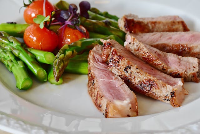 Grilled meat served with cooked asparagus and tomatoes.