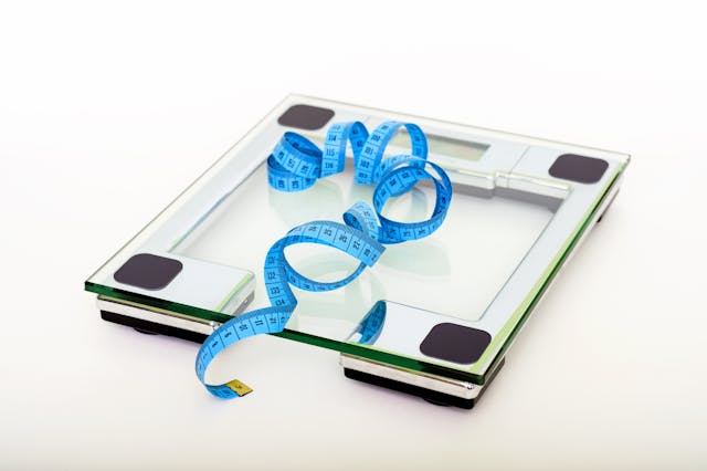 A blue measuring tape laying on top of a glass weighing scale.