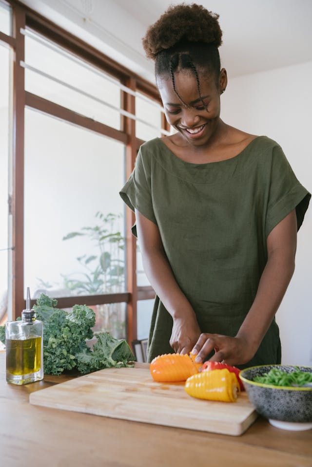 A woman in green dress happily chopping vegetables in her kitchen.