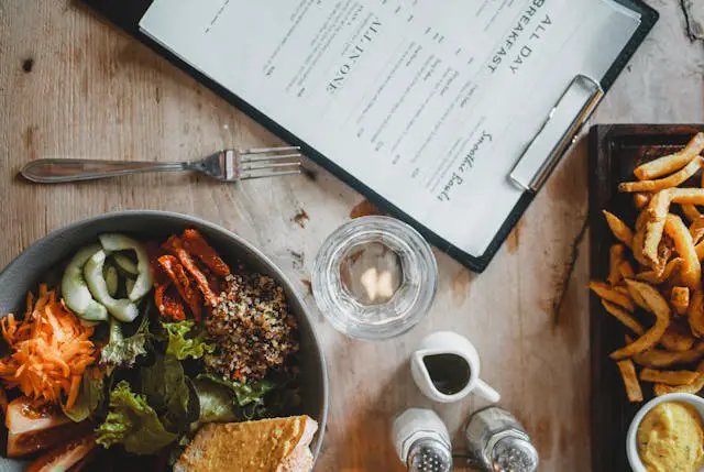 A bowl of salad beside a restaurant menu.