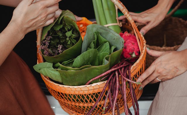 A hand holding a basket of green leafy vegetables.