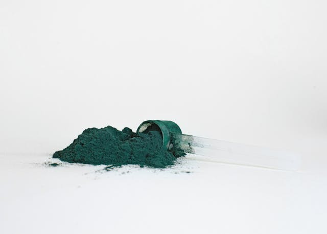 A scoop of green powder scattered on the white surface.