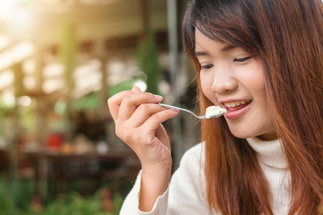 A woman holding up a spoon with a white creamy-looking food.