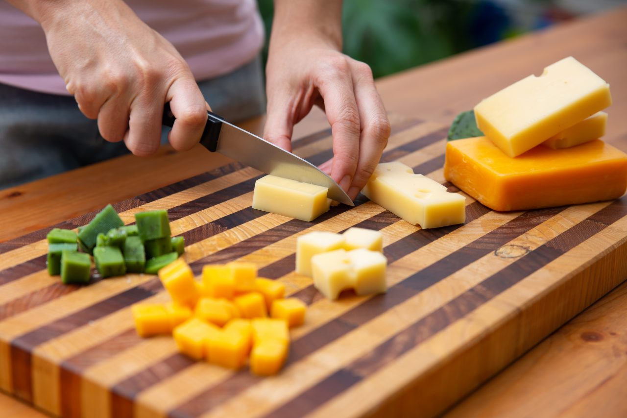 Someone cutting different types of cheese into cubes on a wooden board.